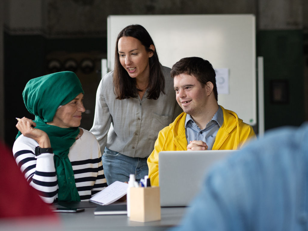A man with Down syndrome smiles as he looks at his notes while engaging in conversation with another person