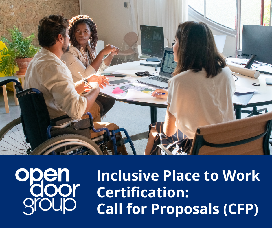 Three individuals engaged in conversation at an office table, with one person seated in a wheelchair participating in the discussion.
